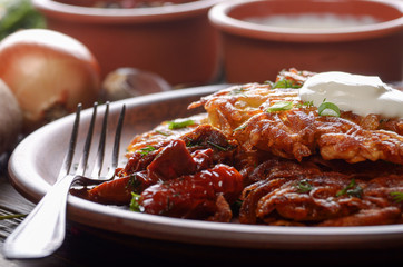 Closeup view at Homemade tasty potato pancakes in clay dish with sun-dried tomatoes and sour creram