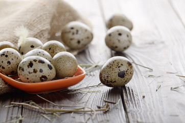 Obraz premium Fresh organic quail eggs in orange clay plate on wooden rustic kitchen table. Space for text