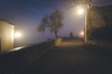 Old European narrow empty street of a medieval town at a foggy evening. Pienza, Italy