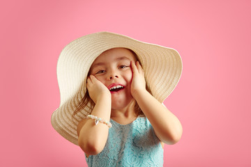 Portrait of surprised girl with open moutn, wears beach hat and beautiful blue dress, expresses joy and happiness, stands over pink isolated background.