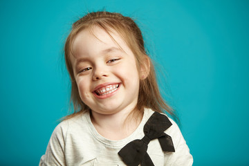 Cute kid girl with a snide smile and low-key laughter stands on blue isolated background.