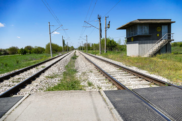 Fototapeta na wymiar Railway electrified line in the plane. Two tracks are lost in the distance. Foreground - rail crossing. End of the rails - a small building.