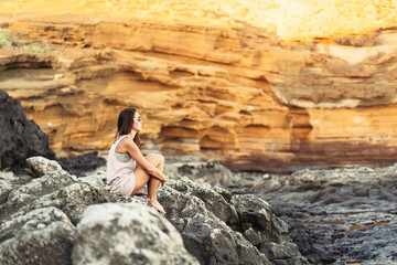 Fototapeta na wymiar Pretty long hair brunette tourist girl relaxing on the stones near sea.