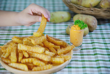 Hand holding delicious fried potato on wooden plate with dipped sauce - traditional fast food concept