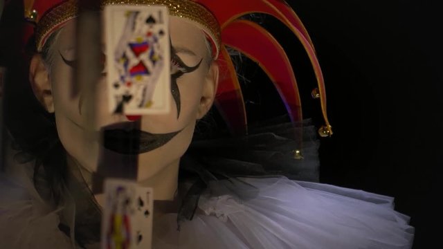 A jester is standing behind the playing cards in the creepy lighting, close up