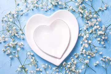 Plates in form of hearts and  fresh white gypsofila  flowers on blue textured background.