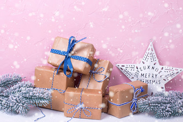 Wrapped boxes with presents, fir tree branches  and Christmas star on white textured background against pink wall.