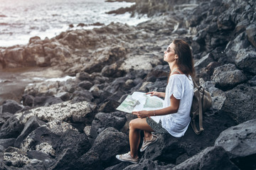 Pretty long hair tourist girl relaxing on the stones near sea.