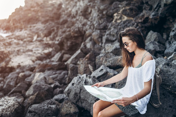 Pretty long hair tourist girl relaxing on the stones near sea.