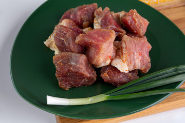 Pickled slices of pork with garlic, pepper, paprika have a beautiful color and lies in a green dish. The meat is prepared for the grill. Appetizing and delicious freshly prepared meat dishes.