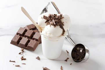 Fresh ice cream sundae with chocolate sprinkles on top, chocolate bar and ice cream spoon on white table,coseup