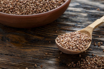 raw buckwheat groats in a clay plate on a wooden background. next to the plate is a wooden spoon.