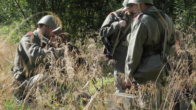 Soldiers rest in meadow one check his machine gun