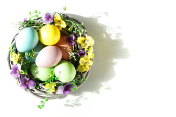 Easter eggs background with copy space. Pastel colored deco eggs and flowers in a wicker basket with sunlights shadows.Copy space