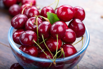 sweet red cherries in a plate on a wooden background.