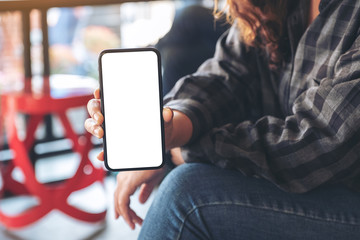 Mockup image of a woman holding and showing black mobile phone with blank white screen in cafe