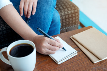 Closeup image of a woman writing on blank notebook with coffee cup on wooden table