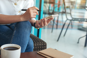 Closeup image of a woman holding and writing on blank notebook with coffee cup on the table