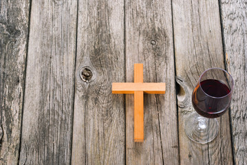 wooden cross and glass of red wine on old wood table
