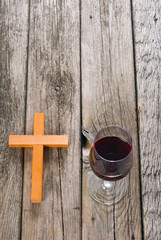 wooden cross and glass of red wine on old wood table