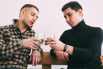 two men drink whiskey sitting on a wooden couch