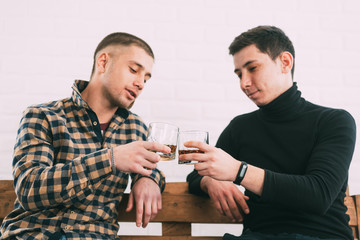 two men drink whiskey sitting on a wooden couch
