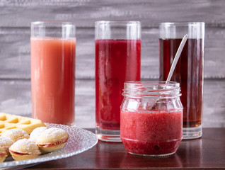 Red juice in a glass next to a bowl of cookies and a small jar of jam.