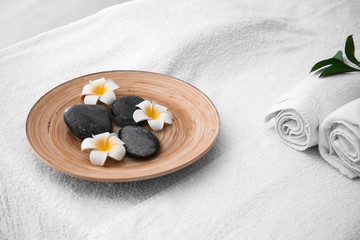 Plate with massage stones and flowers on table in spa salon