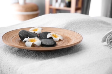 Plate with massage stones and flowers on table in spa salon