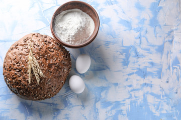 Loaf of tasty bread with flour and eggs on color background