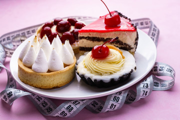 healthy lifestyle, diet, carbs reduce, sugar, sweets. pink background with delicious cakes and measure tape. fitness, nutritionist, dietitian blog design concept