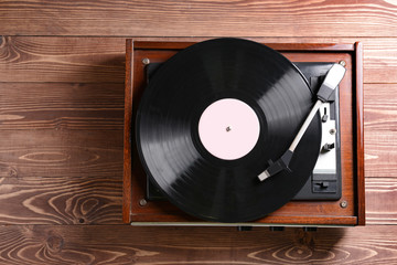 Record player with vinyl disc on wooden table