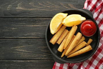 Frying pan with tasty corn cobs, lemon and sauce on wooden table