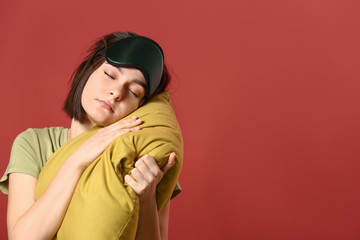 Naklejka premium Sleepy young woman with mask and pillow on color background