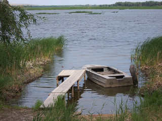 old metal boat is tied at a wooden pier overlooking the river