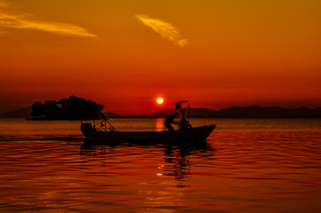 Man driving a boat with the setting sun in the background