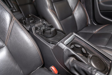 Interior view with leather seats and four cupholders of black used car stands in the showroom after dry washing before sale