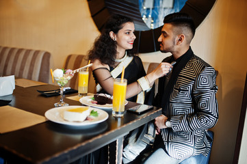 Lovely indian couple in love, wear at saree and elegant suit, posed on restaurant. Woman tied tie on her man.