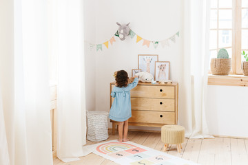 Little girl wearing light blue dress playing in children room scandinavian style.