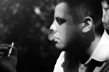 Cool hipster guy is smoking a cigarette outdoors. Bad habits for your health concept.