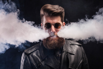 Cigarette smoking coming out of attractive man mouth with cool beard over black background