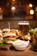 Golden beer next to delicious burgers on wooden table