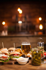 Mini burgers with a big glass of golden beer next to a jar of pickles