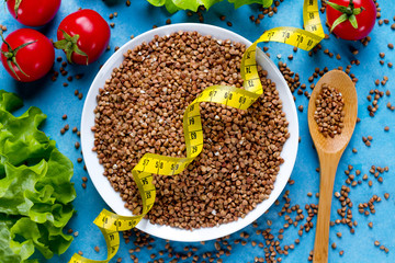 Buckwheat bowl and spoon with fresh ripe vegetables and yellow measuring tape. Buckwheat cereal grains for dietary, healthy eating. Fiber and slimming food. Diet concept. Top view