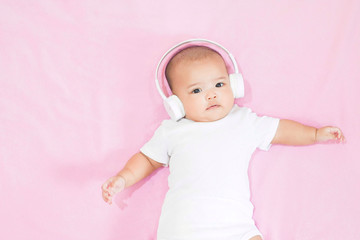 Asian baby girl wears white headphone and white shirt on pink background