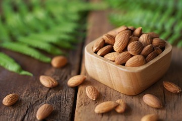 Almond nut in wood bowl on wooden table with green leaf decoration background