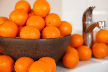 A lot of oranges in a large wooden bowl. Washed oranges next to the water tap. Healthy food and lifestyle