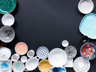 white and colorful tableware in different designs and sizes on black background, photographed from above in daylight