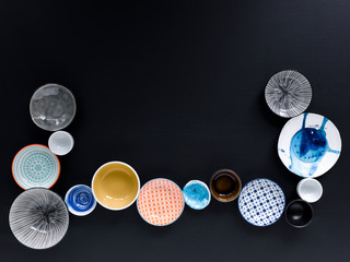 white and colorful tableware in different designs and sizes on black background, photographed from above in daylight