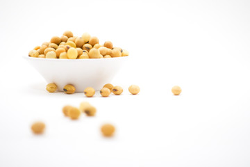 Soy seeds in white bowl and some drop out on white background